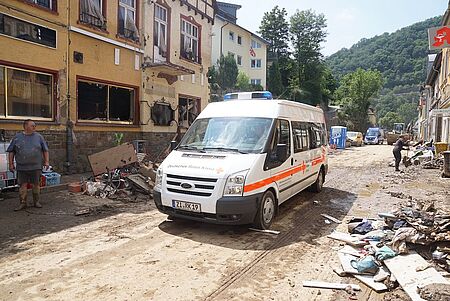 DRK Einsatzfahrzeug fährt durch eine vom Hochwasser zerstörte Strasse im Ahrtal