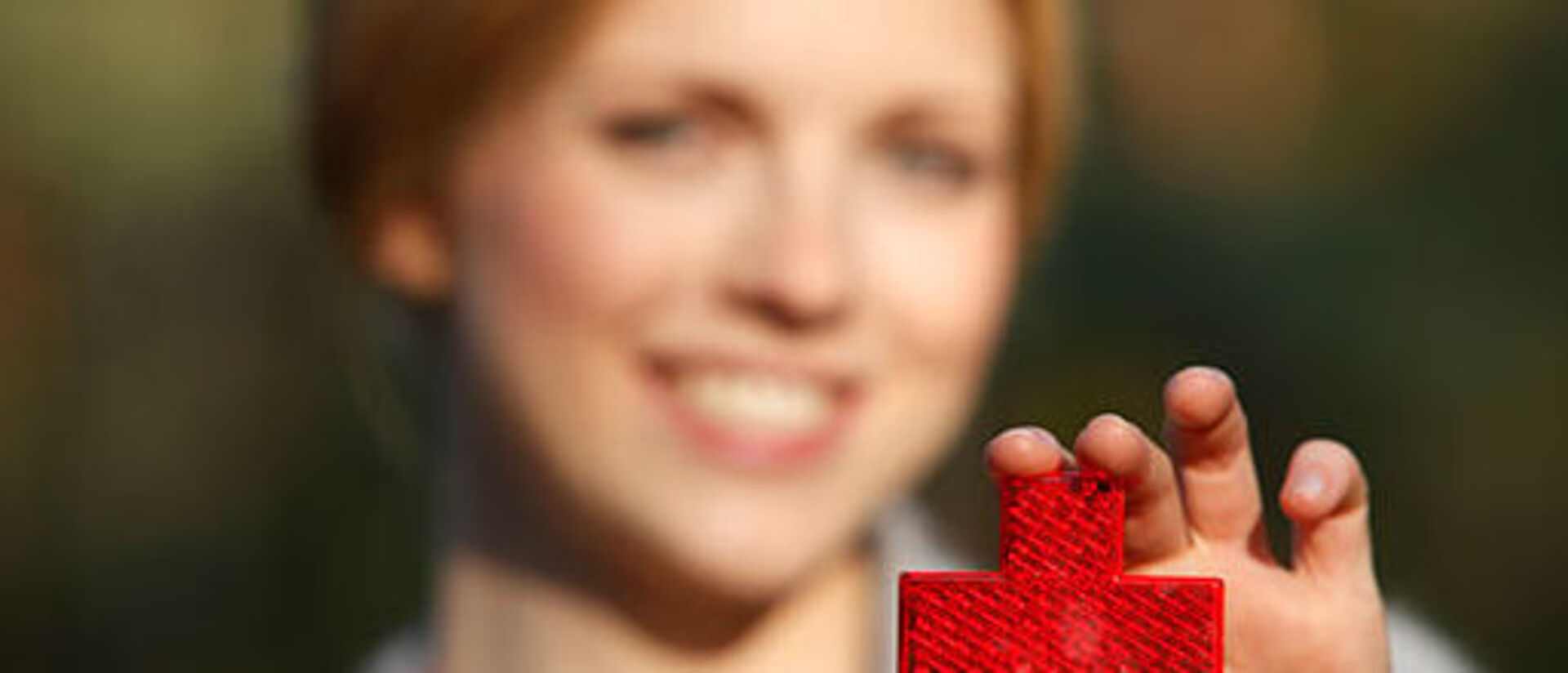 Eine Frau hält ihre ausgestreckte Hand in die Kamera. Darin hält sie ein reflektierendes Rotes Kreuz.