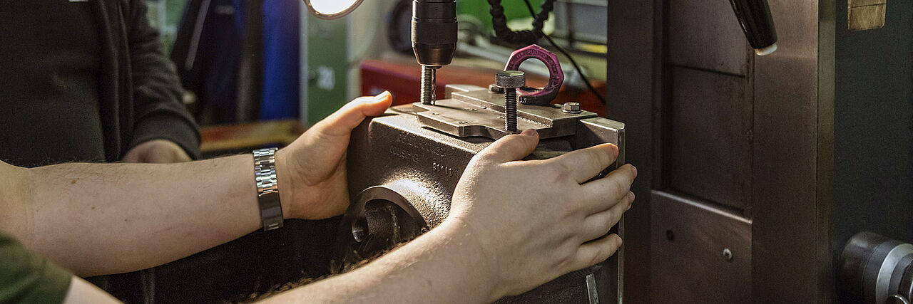 in der Metallwerkstatt bohrt ein Mitarbeiter Löcher in ein Getriebegehäuse