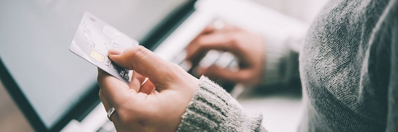 Eine Frau sitzt an ihrem Laptop und hält ihre Bankkarte in der Hand. Sie tippt ihre Kontodaten ab.