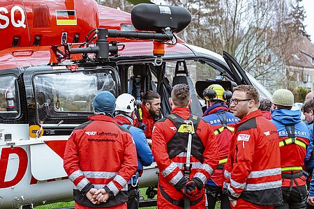 Mehrere Bergretter und Luftretter besprechen gemeinsam einen Einsatz vor einem Hubschrauber.