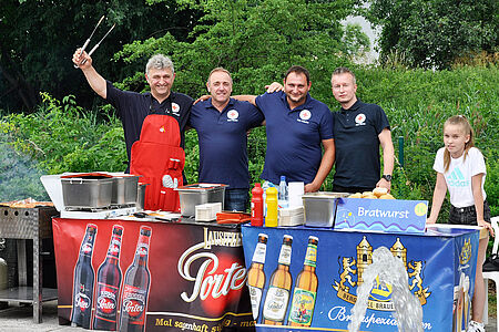 Vier Männer stehen am Grill und kümmern sich um die hungrigen Gäste.