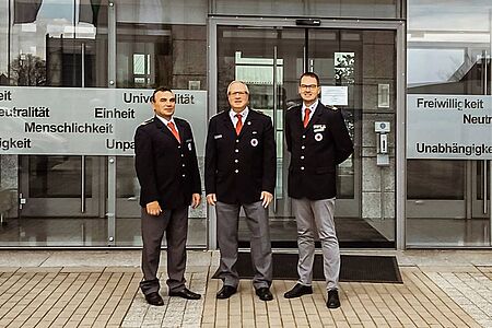 Der neue Landesleiter der Bereitschaften sowie seine zwei Stellvertreter stehen vor dem DRK Zentrum und lächeln in die Kamera.