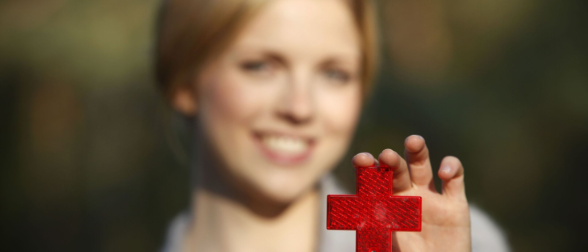 Eine Frau hält ihre ausgestreckte Hand in die Kamera. Darin hält sie ein reflektierendes Rotes Kreuz.