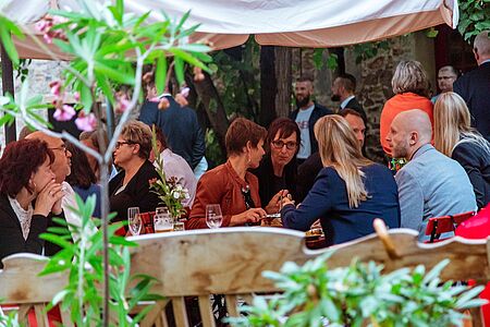 Die Gäste sitzen gemütlich beieinander, essen, trinken und unterhalten sich.